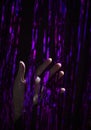 Vertical shot of a hand passing through a purple dynamic lines stripes of garland rain band