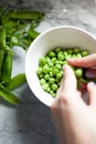 Vertical shot of a hand shelling peas in a white bowl on marble surface Royalty Free Stock Photo