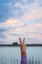 Vertical shot of a hand showing peace sign under a cloudy blue sky Royalty Free Stock Photo