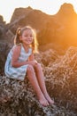 Vertical shot of a happy girl sitting on a rock at a dreamy sunshine