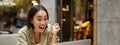 Vertical shot of happy girl talking on video call, looks at laptop, having online meeting, sitting in outdoor cafe Royalty Free Stock Photo