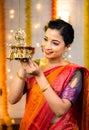 Vertical shot of happy smiling indian girl in traditional wear light up hanging oil lamp during festival at home -