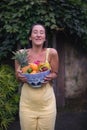 Vertical shot of a happy young woman holding a basket of tropical fruits. Royalty Free Stock Photo