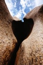 Vertical shot of a heart-shaped hole between rocks under a cloudy blue sky Royalty Free Stock Photo