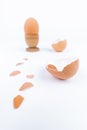Vertical shot hen egg in old wooden egg stand and multiple broken egg shells on a white surface. Minimalism. Conceptual art for