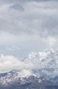 Vertical shot of a high rocky mountain covered with snow under a cloudy sky Royalty Free Stock Photo