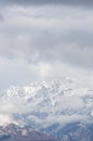 Vertical shot of a high rocky mountain covered with snow under a cloudy sky Royalty Free Stock Photo