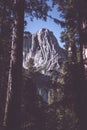 Vertical shot of a high rocky mountain surrounded by green trees under the beautiful blue sky Royalty Free Stock Photo