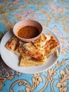 Vertical shot of a hot roti canai served with bowl of curry on a patterned tablecloth