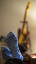 Vertical shot of human feet in blue socks on a blurred background of an electric guitar