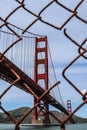 A vertical shot of the Golden Gate Bridge visible through a rusty fence at Fort Point Royalty Free Stock Photo