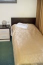 Vertical shot of the interior of the hotel bedroom with an empty single bed with wooden headboard and bedside table and towels on