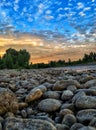 Vertical shot of the jetty rocks of a river with trees in the background during the sunset