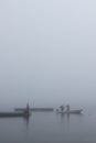 Vertical shot of a lake with a dock and people on the boat on a foggy day