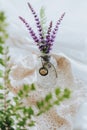 Vertical shot of lavender plants in a small transparent vase with a necklace on a nude fabric