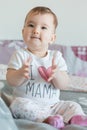 Vertical shot. Little baby smiling sits on bed at home