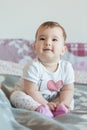 Vertical shot. Little baby smiling sits on bed at home