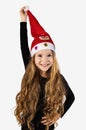 Vertical shot of a little girl dressed in black overalls smiling attractively Holding the top of her Santa hat with one Royalty Free Stock Photo