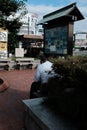 Vertical shot of a lonely male sitting on a bench near green plants during daytime under cloudy sky