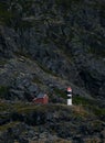Vertical shot of the Lyngstuva lighthouse and a red small house situated on a rocky mountain, Norway