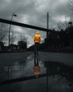 Vertical shot of a male from behind walking on the street with visible reflection on the rainwater