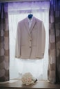 Vertical shot of a male cream suit hung from the window and the flower bouquet on the