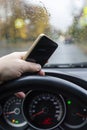 Vertical shot male hand with smartphone on steering wheel of car