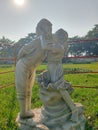 Vertical shot of a marble sculpture of a little girl kissing a boy in the garden.