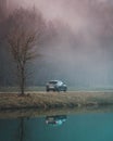 Vertical shot of a Mazda CX-3 reflected in the lake, against a foggy forest landscape