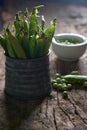 Vertical shot of a metal basket with pea pods and a bowl of peas on wooden table in the background Royalty Free Stock Photo