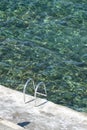 Vertical shot of a metal ladder leading into a clear seawater pool Royalty Free Stock Photo