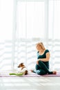 Vertical shot of middle age woman in sportswear channels serious expression while sitting on yoga mat with her dog Royalty Free Stock Photo