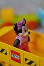 Vertical shot of Minnie Mouse standing on a yellow lego car and in a pink dress and a pink bow