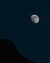 Vertical shot of the moon in a dark blue sky with a silhouetted mountain in the foreground