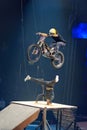 Vertical shot of a motorcyclist jumping over a parkour athlete on a ramp.