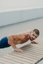 Vertical shot of muscular bearded man stands in plank pose trains chest and arms muscles has hard workout for keeping athletic