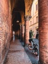 Vertical shot of narrow street with parked bicycle between old columns in Bologna, Italy