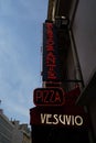 Vertical shot of a neon Pizza sign on a building with a blue sky background