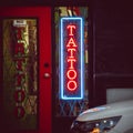 Vertical shot of a neon tattoo salon sign on a door illuminated at night