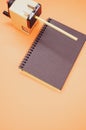 Vertical shot of a notebook and a mechanical pencil sharpener on an orange surface