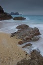 vertical shot of ocean shore and waves crashing on rocks with cliffs and gray sky in the background Royalty Free Stock Photo