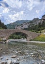 Vertical shot of the old Bridge of Bujaruelo over a clear river with mountains in the background