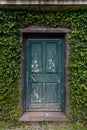 A vertical shot of an old green door in a wall lined with ivy plants Royalty Free Stock Photo