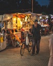 Vertical shot of an old man with a bicycle next to small markets during the festival at night