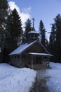 Vertical shot of an old russian traditional small wooden church covered in snow on a background of pine trees and spruces. Shot in Royalty Free Stock Photo