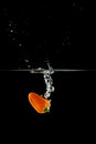 Vertical shot of an orange bell pepper dropping into the water with splashes on a black background Royalty Free Stock Photo