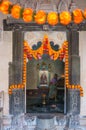 Vertical shot of orange flowers around the entrance to an Indian temple with a woman cleaning inside