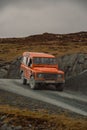 Vertical shot of an Orange Land rover Defender located on a gravel path in the nature