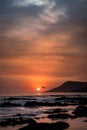 Vertical shot of an orange sunset with silhouette of hills on the beach