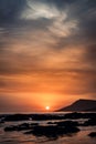 Vertical shot of an orange sunset with silhouette of hills on the beach